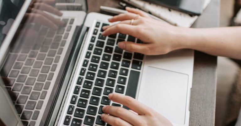 Remote Jobs - From above of unrecognizable woman sitting at table and typing on keyboard of computer during remote work in modern workspace