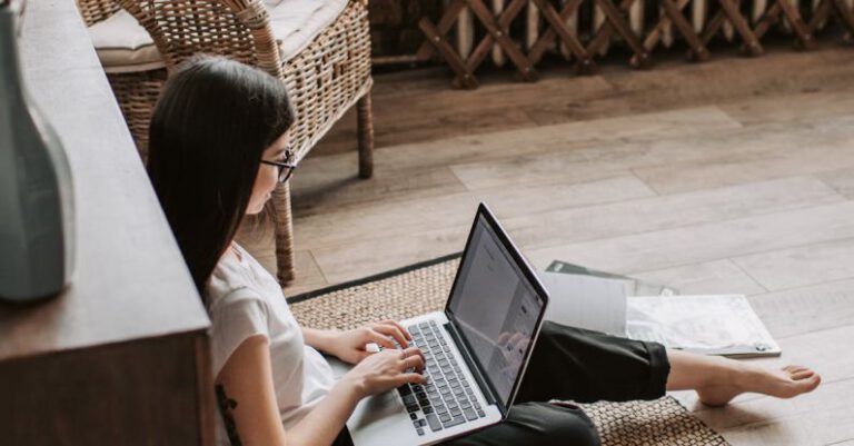 Programs - Young barefoot woman using laptop on floor near books in stylish living room